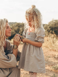 Angi handing flowers to little girl in a meadow, both wearing the Adeline dress in sea foam gray.