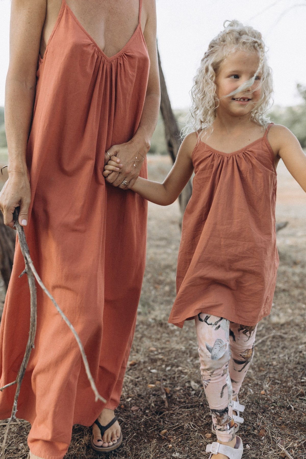 Little girl and mother walking in a field while holding hands and wearing the Adeline dress in rose color.